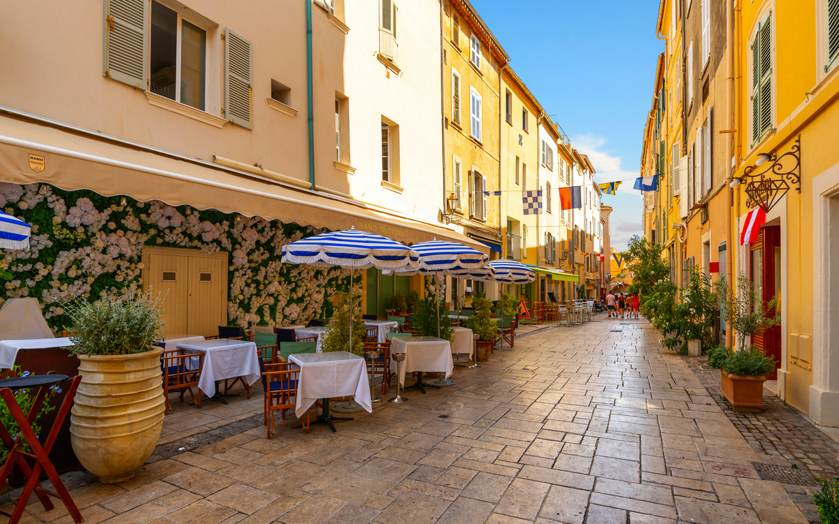 Gasse mit Geschäften und Straßencafés in der farbenfrohen Altstadt der Mittelmeer-Ferienstadt Saint-Tropez in Frankreich an der Côte d'Azur